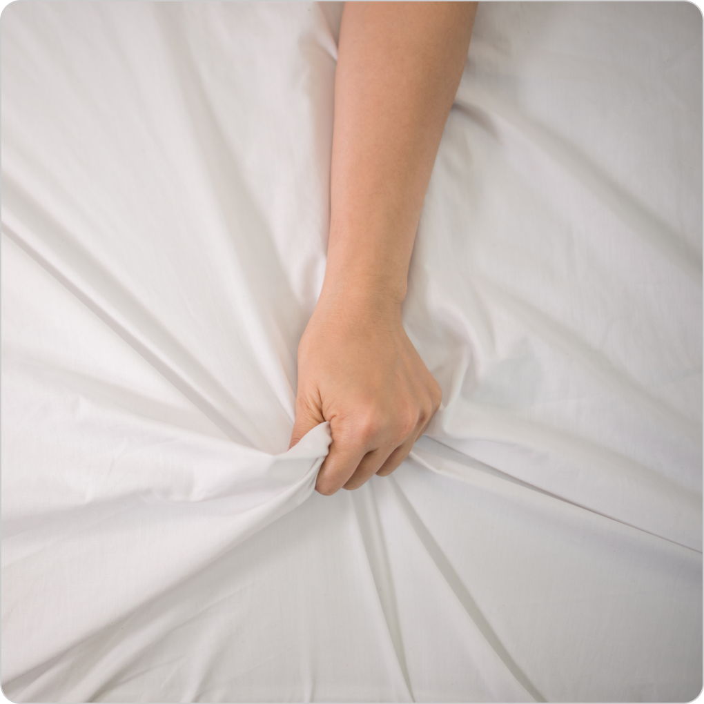 Woman's hand gripping sheets conveying sexual pleasure